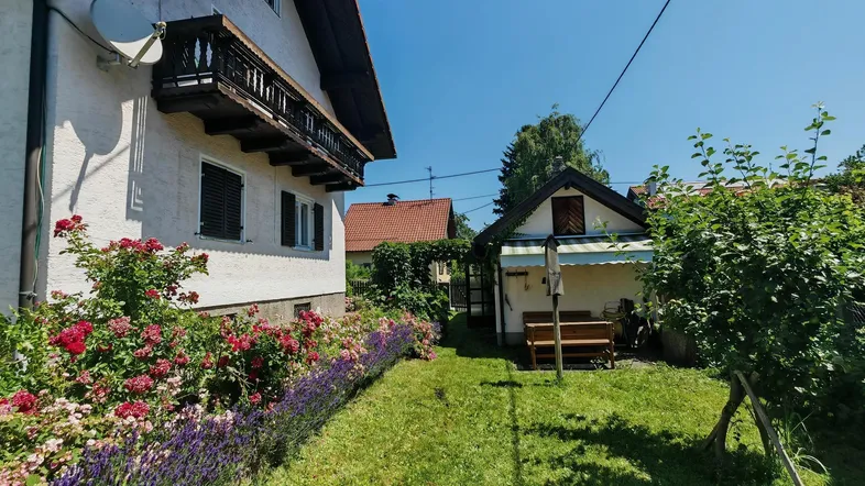 Gepflegter Gartenbereich mit Rasenfläche, blühenden Blumenbeeten und einem traditionellen Balkon am Haus.