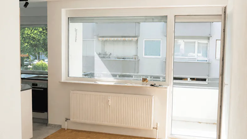 Helles Wohnzimmer mit Parkettboden, großem Fenster und Zugang zu einem Balkon, ideal für gemütliche Stunden.