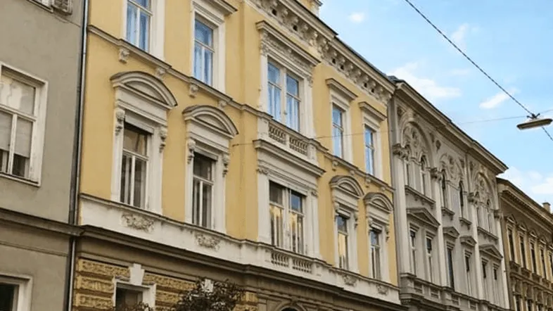 Historisches Gebäude mit gelber Fassade und reich verzierten Fenstern unter blauem Himmel.