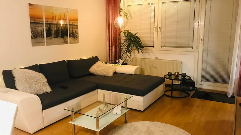 Gemütliches Wohnzimmer mit L-förmigem Sofa, Holzboden und dekorativer Lichterkette.