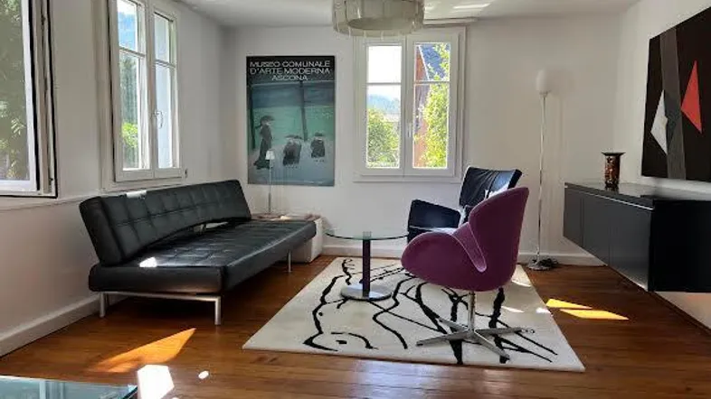 Helles Wohnzimmer mit Holzboden, modernem Sofa und Blick ins Grüne durch große Fenster.