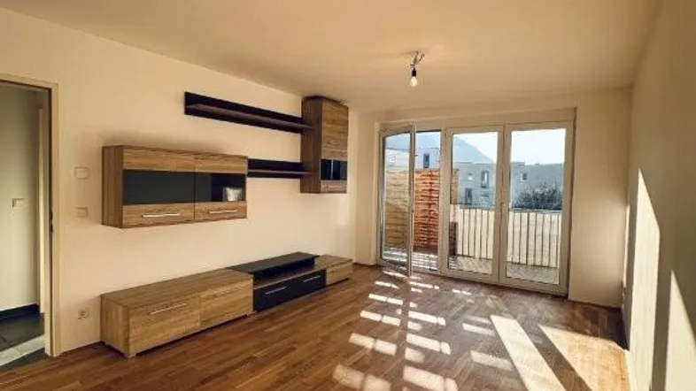 Helles Wohnzimmer mit Holzboden, moderner Wandgestaltung und Zugang zu einem Balkon.