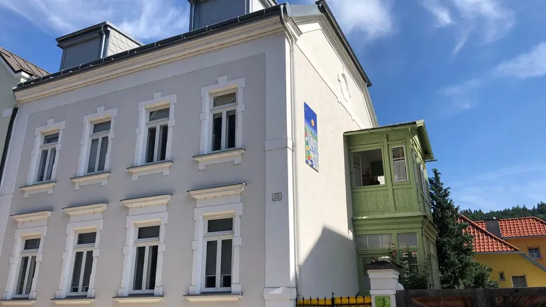 Historisches Gebäude mit heller Fassade, grünen Fensterläden und Dachgauben unter blauem Himmel.