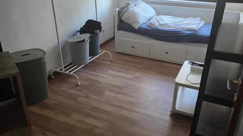 Helles Schlafzimmer mit Einzelbett, Kleiderstange und Laminatboden, ideal für Gäste oder Kinder.
