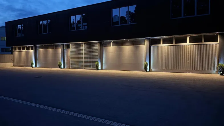 Moderne Gewerbefassade bei Nacht mit beleuchteten Garagentoren und Fenstern im Obergeschoss.