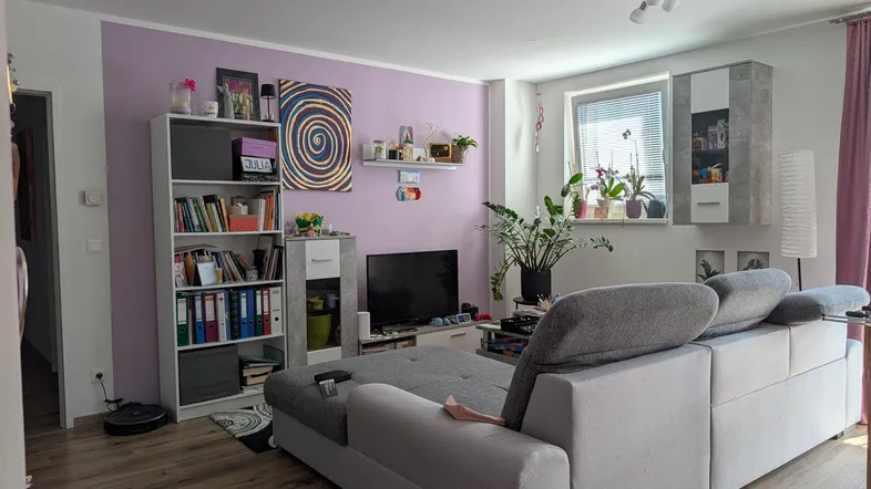 Helles Wohnzimmer mit bequemer Couch, Fernseher und Regalen, ideal zum Entspannen.