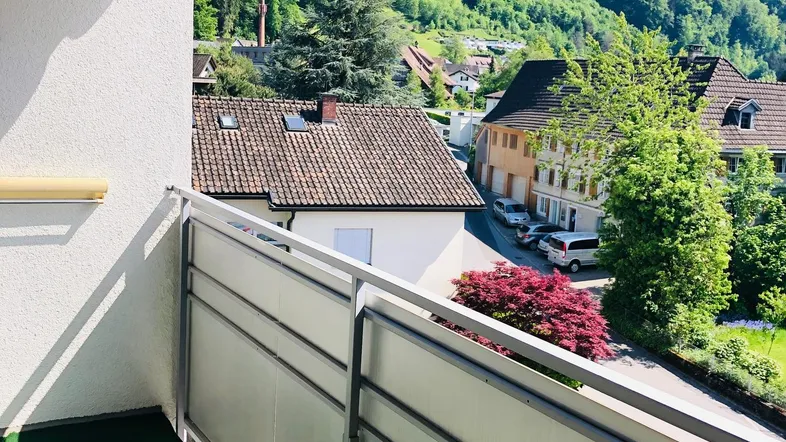 Heller Balkon mit orangefarbener Markise und weitem Blick auf die grünen Berge und das Tal.