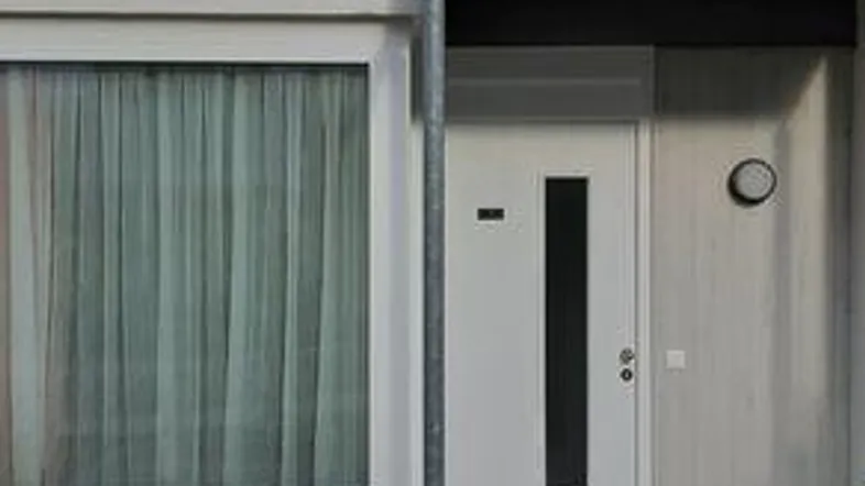 Moderne Gebäudefassade mit Eingangsbereich und kleinem Balkon im oberen Stockwerk.