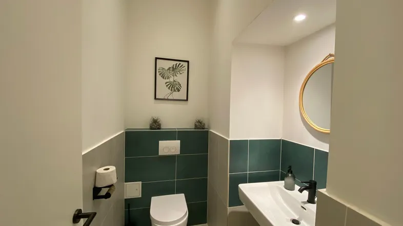 Modernes Gäste-WC mit Wand-WC, Einzelwaschbecken und stilvollen Fliesen in Grau und Dunkelgrün.