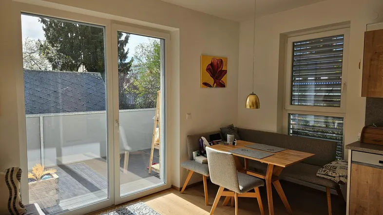 Lichtdurchfluteter Wohn-Essbereich mit Holzküche, Esstisch und Zugang zu einem sonnigen Balkon.