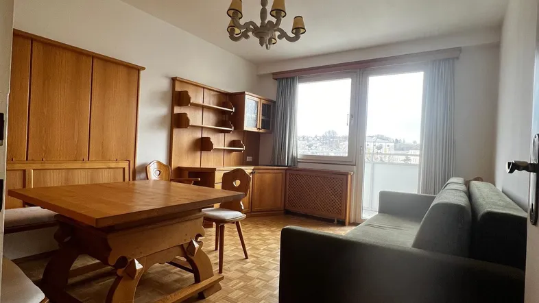 Gemütlicher Wohn-Essbereich mit traditionellen Holzmöbeln, Parkettboden und Zugang zum Balkon.