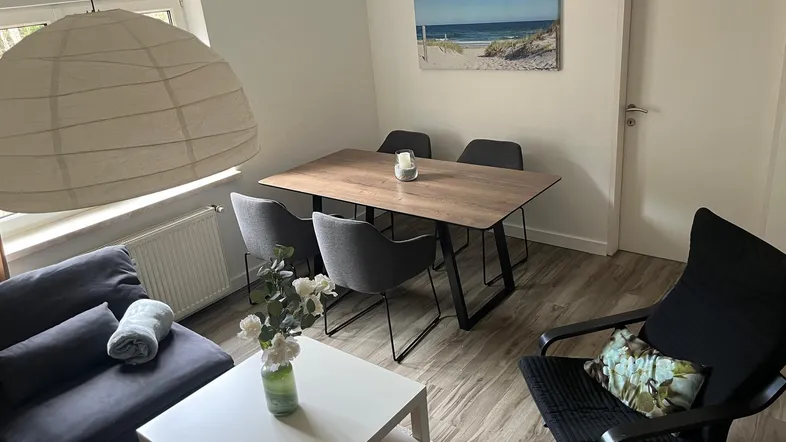 Gemütlicher Wohn- und Essbereich mit modernem Esstisch, bequemer Couch und hellem Laminatboden.