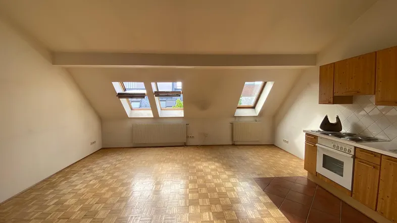 Helles Dachgeschosszimmer mit schrägen Wänden, Parkettboden und integrierter Küchenzeile.