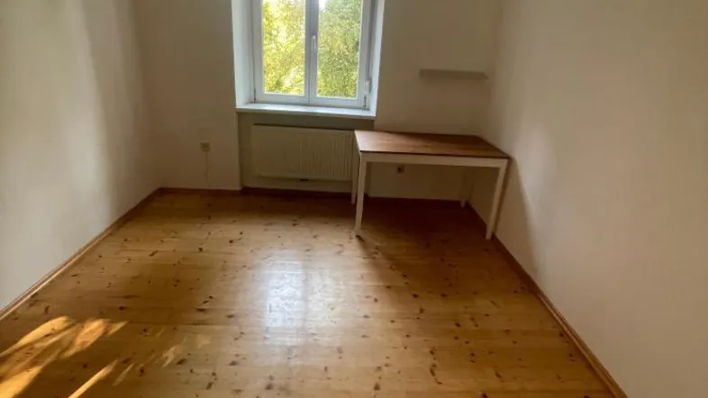 Helles Schlafzimmer mit Holzdielenboden, einem Fenster und Blick ins Grüne.