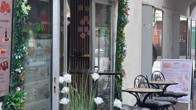Eingangsbereich eines Cafés mit Außensitzplätzen und floraler Dekoration an der Fassade.