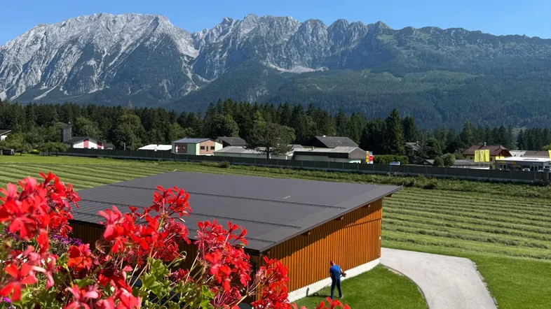 Bergblick mit blühenden roten Geranien und einem Gebäude im Vordergrund unter blauem Himmel.