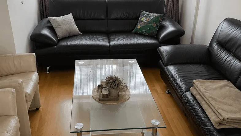 Gemütliches Wohnzimmer mit zwei schwarzen Ledersofas, einem Glastisch und hellem Parkettboden.