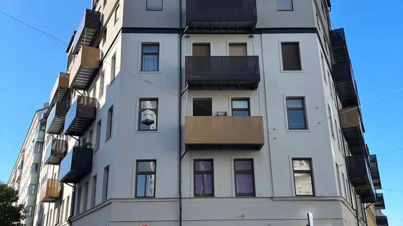 Mehrstöckiges Wohngebäude mit modernen Balkonen und hellgrauer Fassade in städtischer Umgebung.