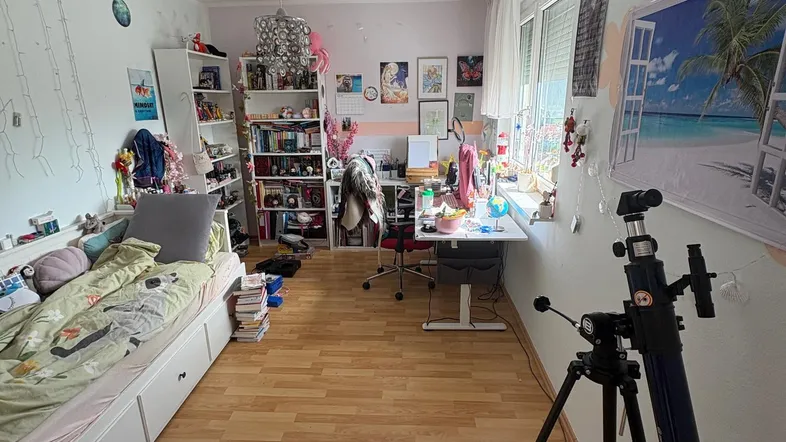 Helles Schlafzimmer mit Holzboden, Bett und Schreibtisch, dekoriert mit persönlichen Gegenständen.