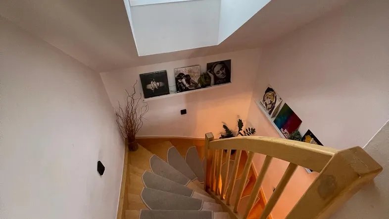 Helles Treppenhaus mit Holzstufen, Teppichläufern und einem Dachfenster für natürliches Licht.