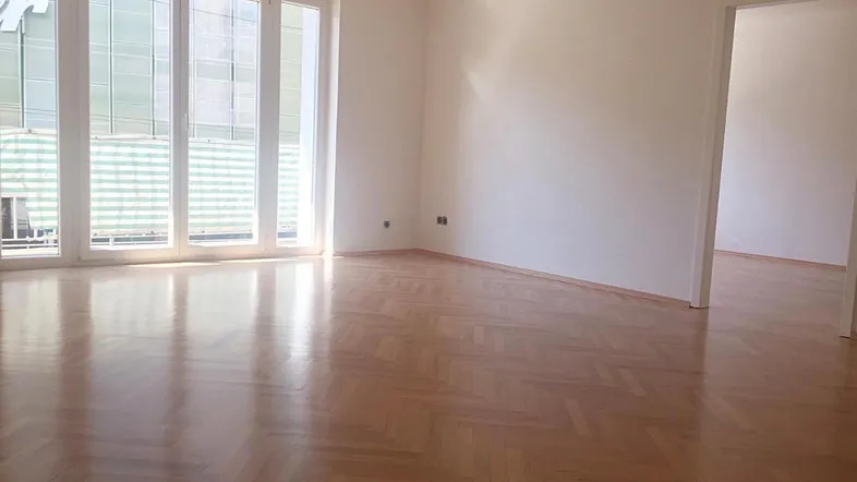 Helles Wohnzimmer mit Fischgrätparkett und großen Fenstern, bereit für die Einrichtung.