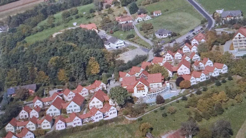 Luftaufnahme einer Ferienanlage mit vielen kleinen Häusern, einem Pool und grüner Umgebung.