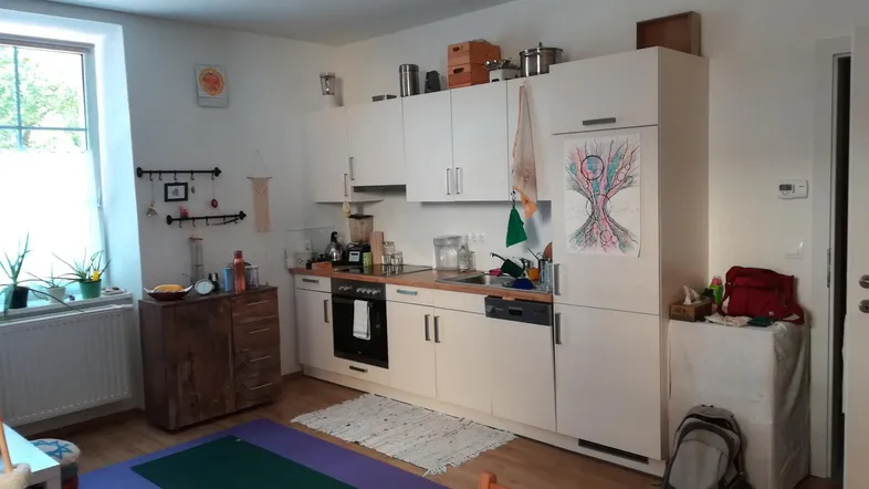 Helle Küche mit weißen Schränken, Holzboden und einem Fenster, das viel Tageslicht hereinlässt.