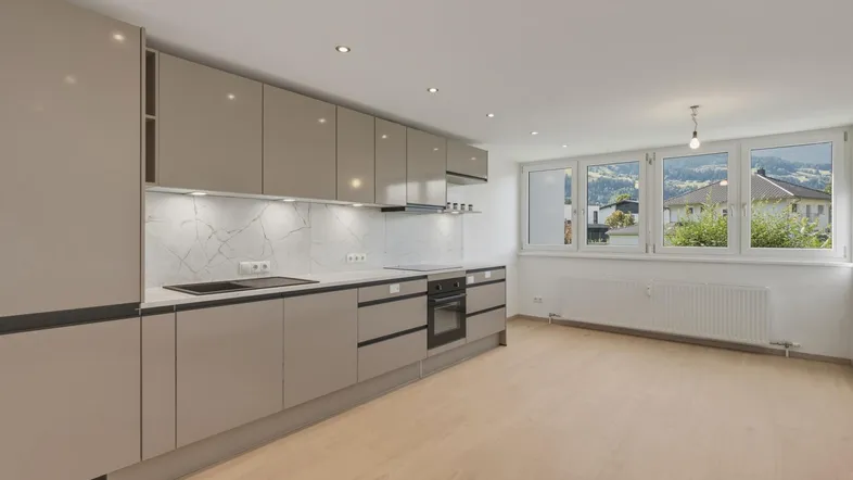 Moderne Küche mit hellgrauen Schränken, Marmor-Rückwand und Blick auf grüne Hügel.