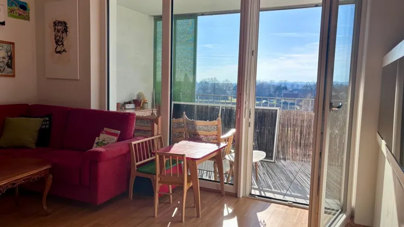 Helles Wohnzimmer mit rotem Sofa, Holzboden und Zugang zu einem sonnigen Balkon mit Weitblick.