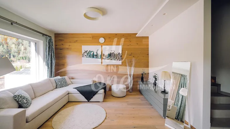 Helles Wohnzimmer mit großem Sofa, Holzwandverkleidung und Blick ins Grüne.
