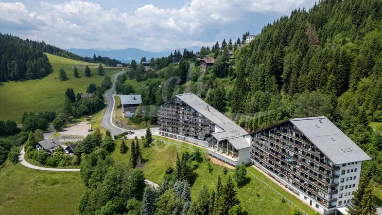Luftaufnahme von modernen Apartmentgebäuden in einer grünen Berglandschaft unter blauem Himmel.
