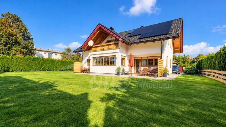 Großzügiger Gartenbereich mit gepflegtem Rasen und einem Einfamilienhaus mit Solaranlage.