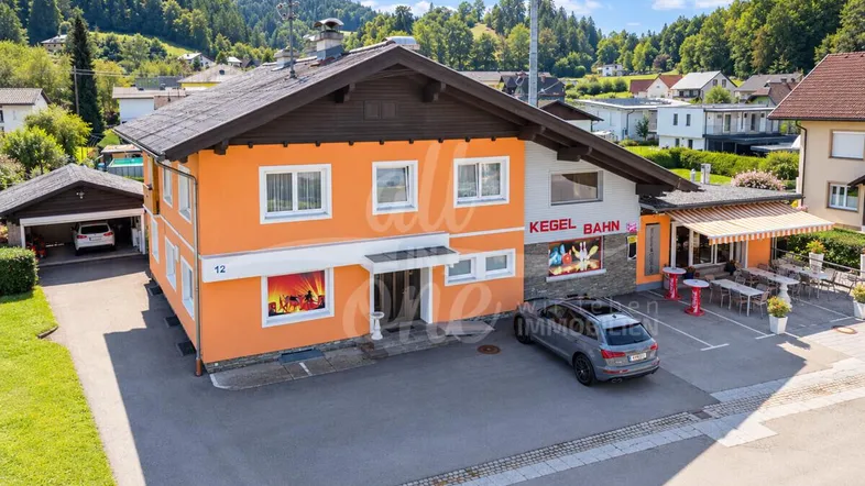 Großes Gebäude mit orangefarbener Fassade, Parkplätzen und einem Carport in ländlicher Umgebung.