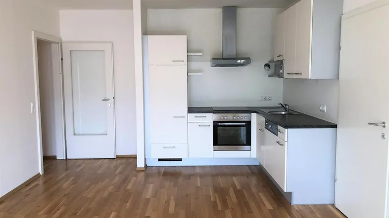 Leere Küche mit weißen Schränken, dunkler Arbeitsplatte und Holzboden, bereit zur Nutzung.