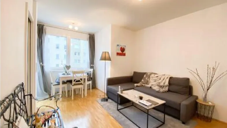 Helles Wohn- und Esszimmer mit Parkettboden, bequemer Couch und Esstisch am Fenster.