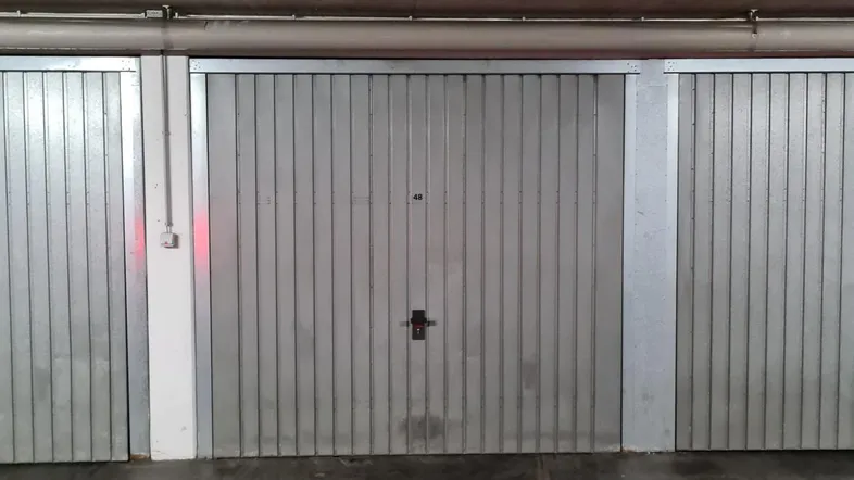 Reihen von geschlossenen Garagentoren in einer Tiefgarage mit Betonboden und -decke.