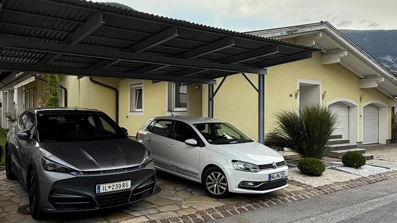 Gelbe Hausfassade mit modernem Carport und gepflasterter Einfahrt.