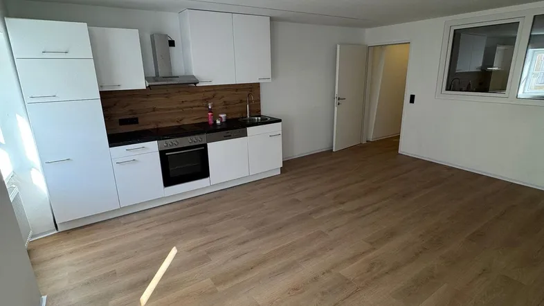 Moderne Küchenzeile mit weißen Schränken, Holzarbeitsplatte und Laminatboden in einem hellen Raum.