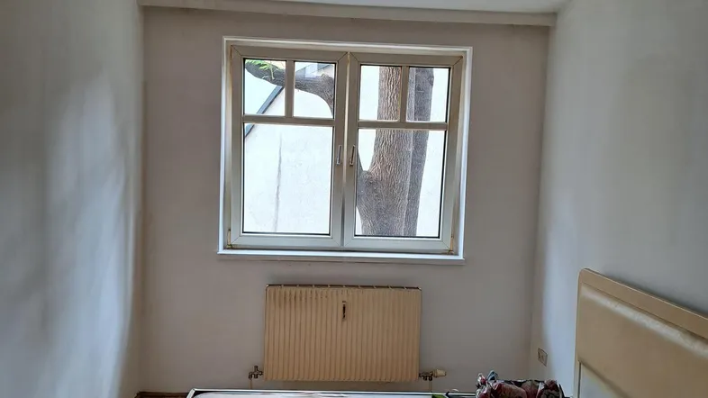 Helles Schlafzimmer mit Holzboden, Fenster und Heizkörper, bereit zur Einrichtung.