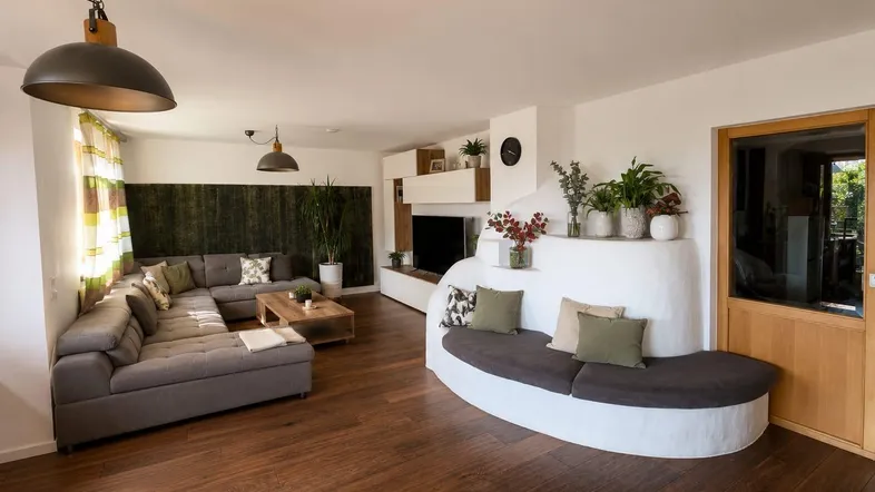 Geräumiges Wohnzimmer mit gemütlicher Sitzecke, Holzboden und integrierter Ofenbank.