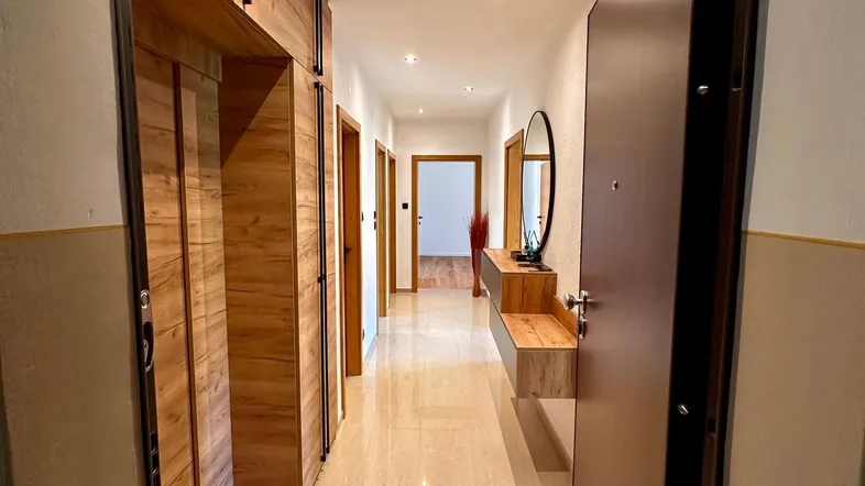 Langer, heller Flur mit Holzverkleidung, Einbauschränken und einem modernen Wandspiegel.