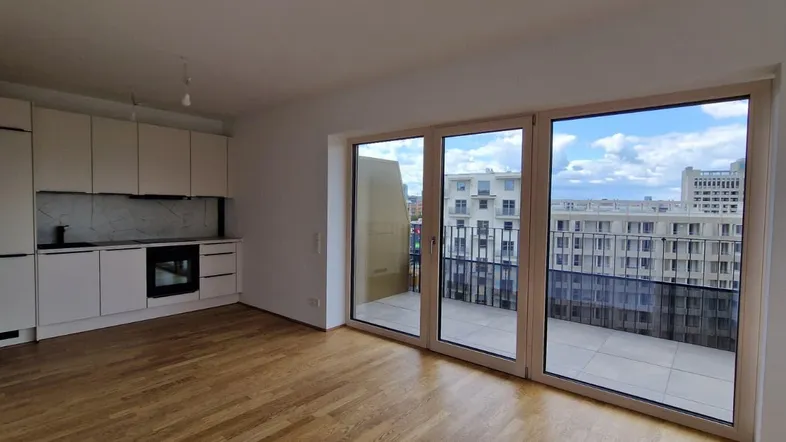 Heller offener Wohnbereich mit integrierter Küche, Holzboden und Zugang zum Balkon mit Stadtblick.