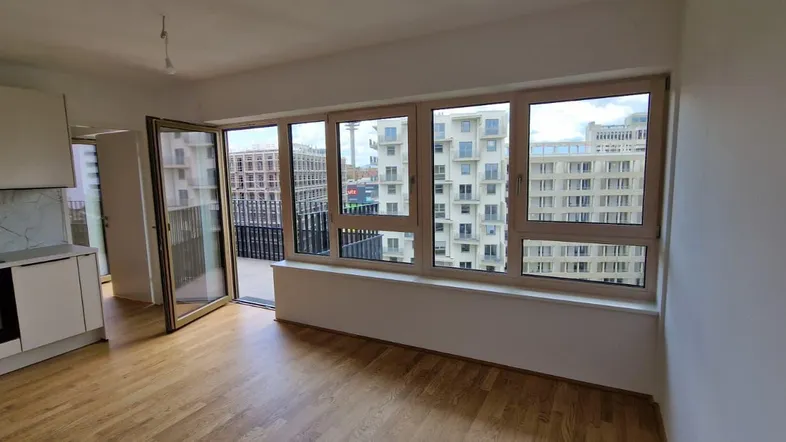 Heller Wohnbereich mit integrierter Küchenzeile, Holzboden und Zugang zu einem Balkon mit Stadtblick.