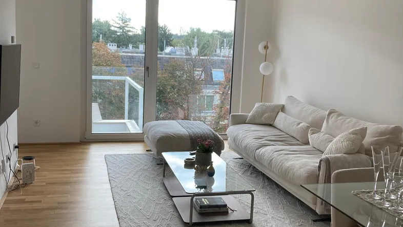 Helles Wohnzimmer mit Holzboden, großem Sofa und Zugang zu einem Balkon mit Stadtblick.