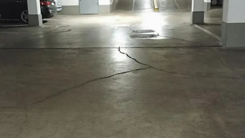 Tiefgarage mit Betonboden, sichtbaren Rissen und einer Zufahrtsrampe zu weiteren Parkebenen.