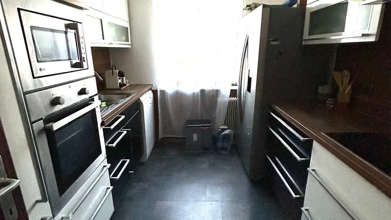 Schmale Küche mit weißen Schränken, dunklen Arbeitsplatten, Einbaugeräten und einem Fenster am Ende.