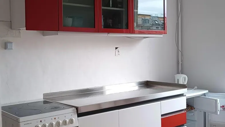 Funktionale Küche mit roten und weißen Schränken, Edelstahl-Arbeitsplatte und Holzfußboden.