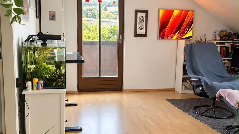 Helles Wohnzimmer mit Holzboden, Aquarium und Zugang zu einem Balkon mit grüner Aussicht.