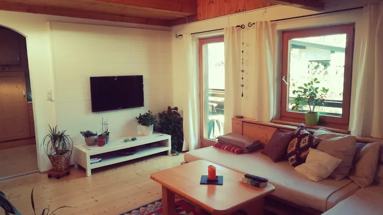 Gemütliches Wohnzimmer mit Holzbalkendecke, Parkettboden und Zugang zum Balkon.