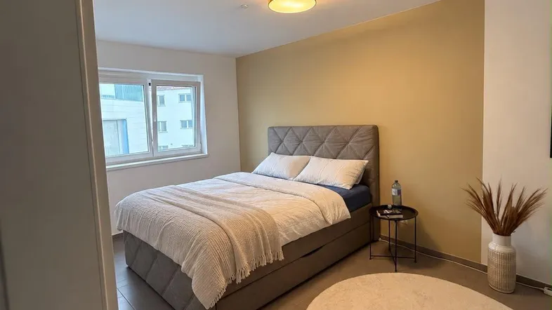 Helles Schlafzimmer mit modernem Bett, beiger Akzentwand und Fliesenboden.